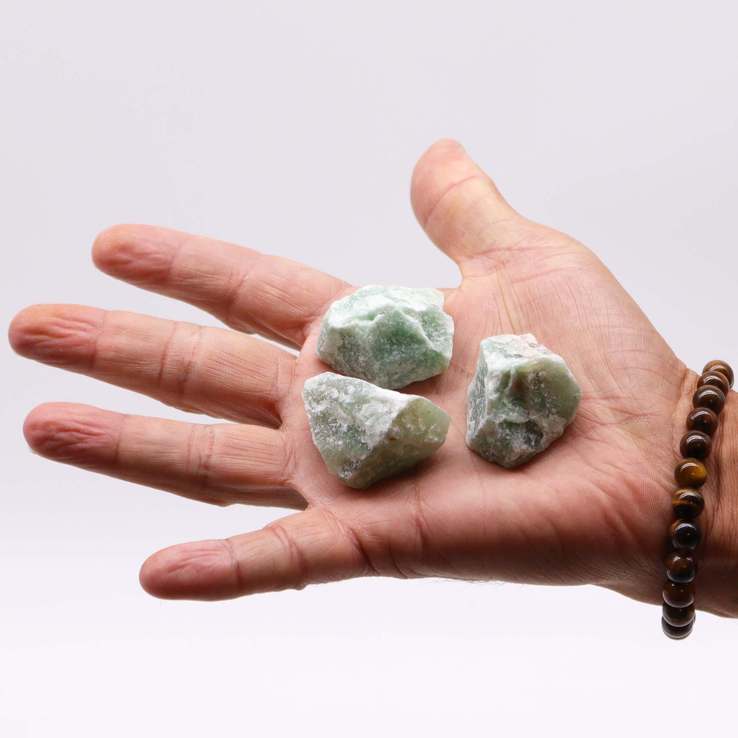 Three pieces of 500g crystal jade for healing displayed on a hand, showcasing natural texture and colors.