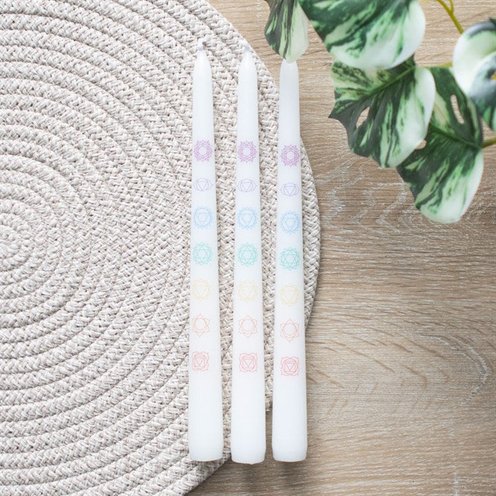 Set of 3 chakra balancing candles set with pastel colors and chakra symbols, placed on a textured mat