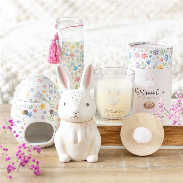 Hot cross bun candle in a glass jar surrounded by a cute rabbit figurine and floral decor, enhancing nostalgic aromas