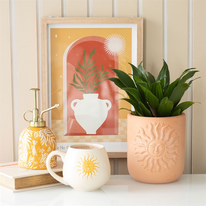 Vase wall art print featuring a potted plant and warm colors, framed and displayed on a wooden table alongside decorative items