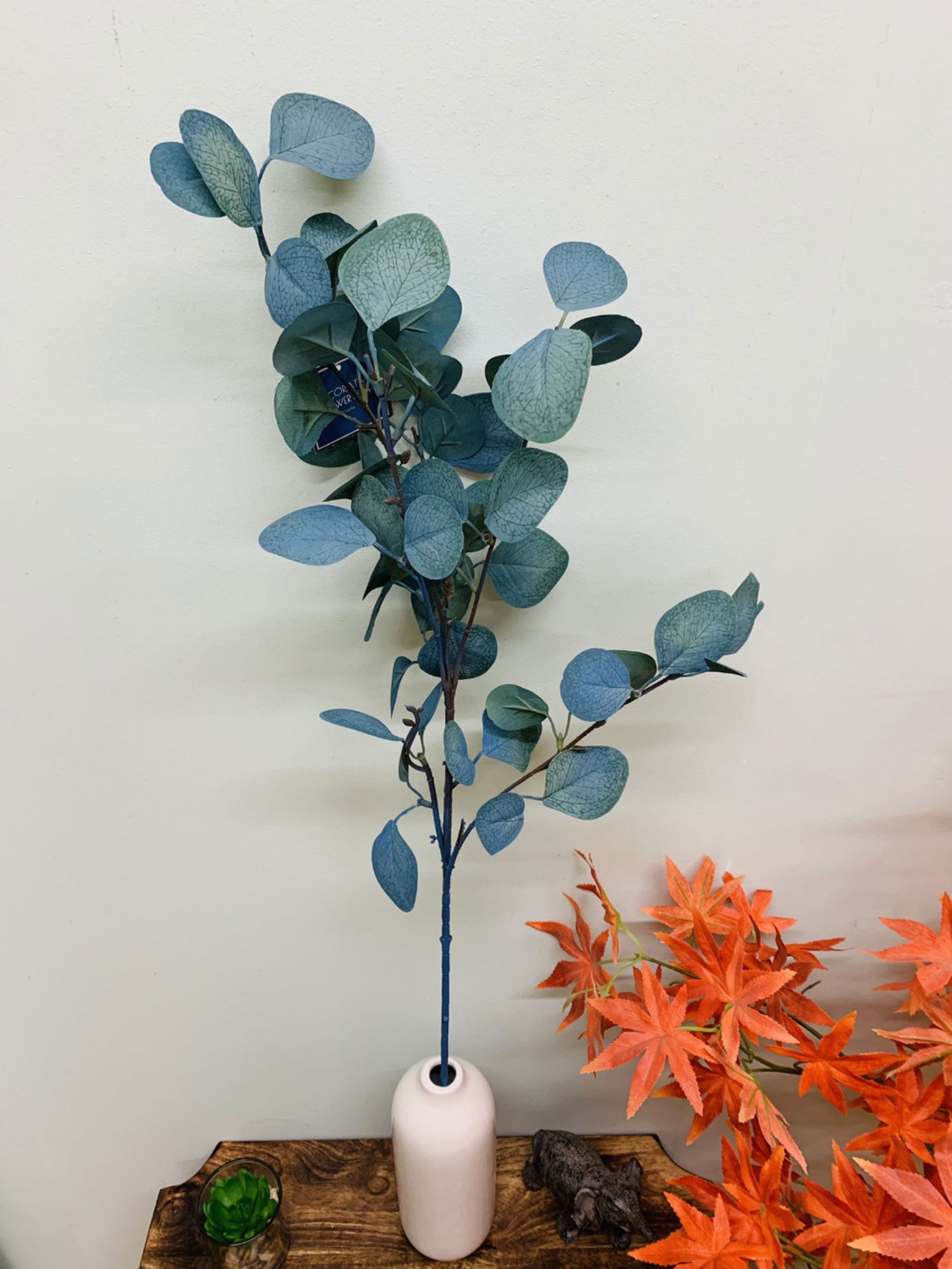 Artificial eucalyptus for spiritual decor in white vase displayed on wooden table with autumn leaves