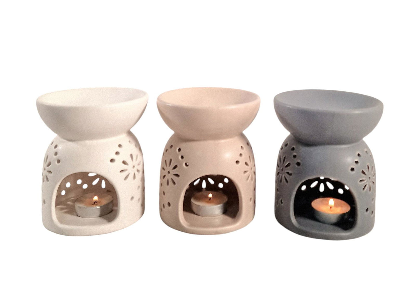 Beige oil burner with pattern displayed alongside white and gray ceramic oil burners with lit candles