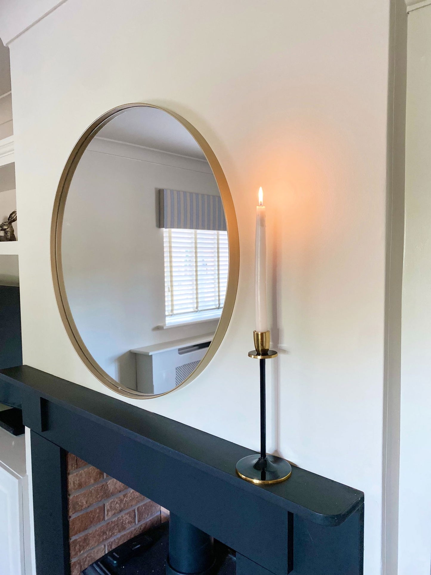 Black and gold candlestick holding a lit taper candle on a dark mantel beneath a round gold-framed mirror