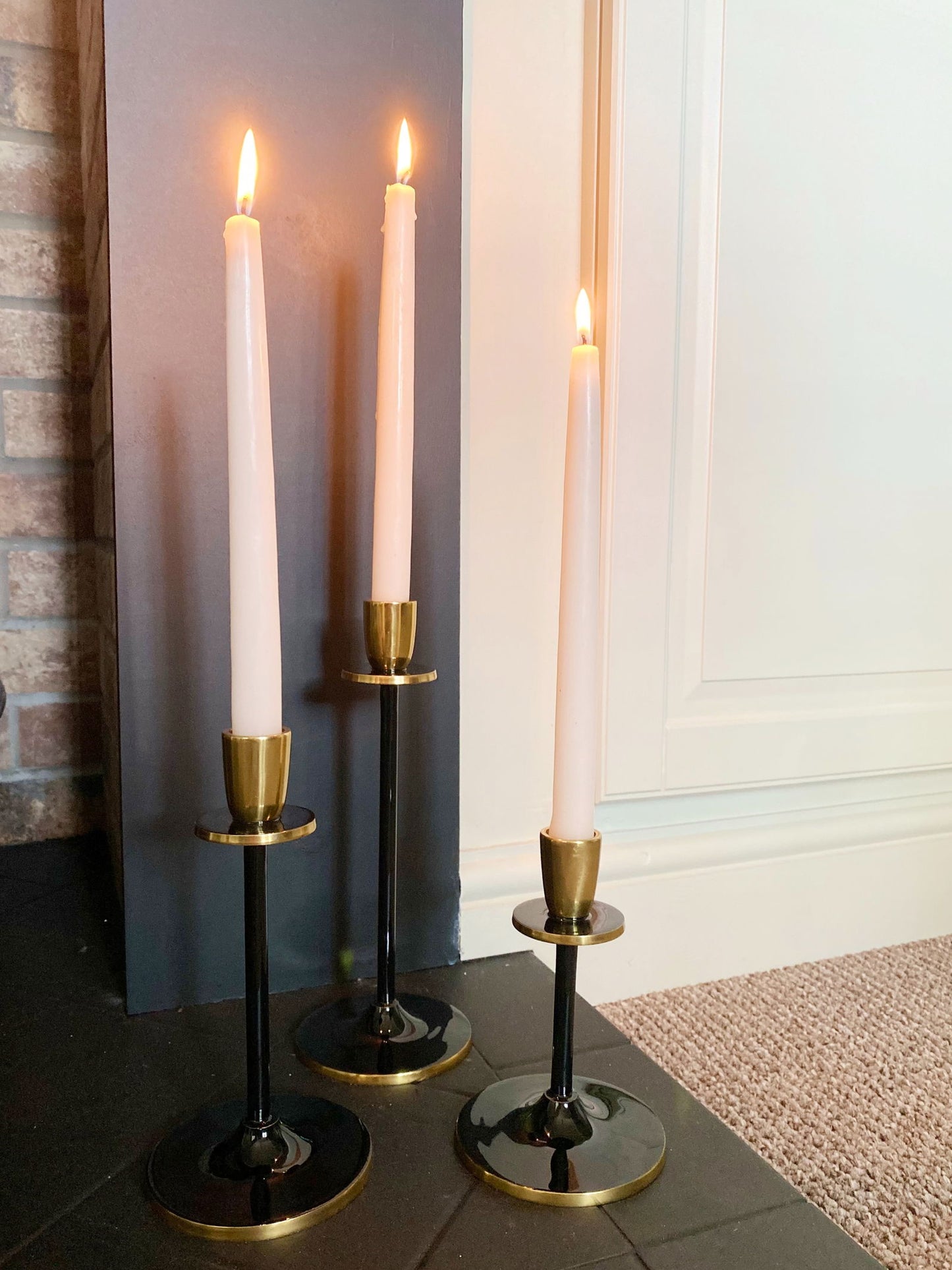 Set of three black and gold candlestick holders with lit white taper candles on floor
