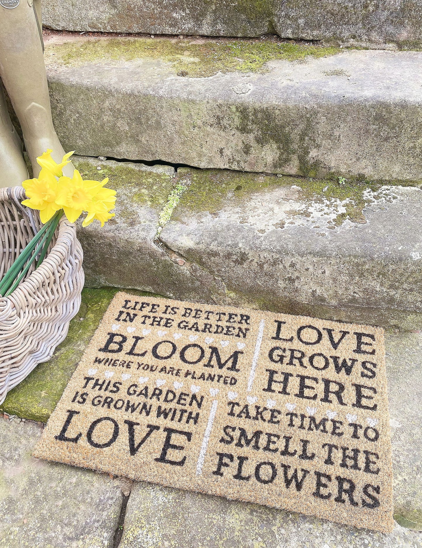Geko Products bloom potting shed doormat with garden quotes placed on stone steps next to basket and yellow flowers