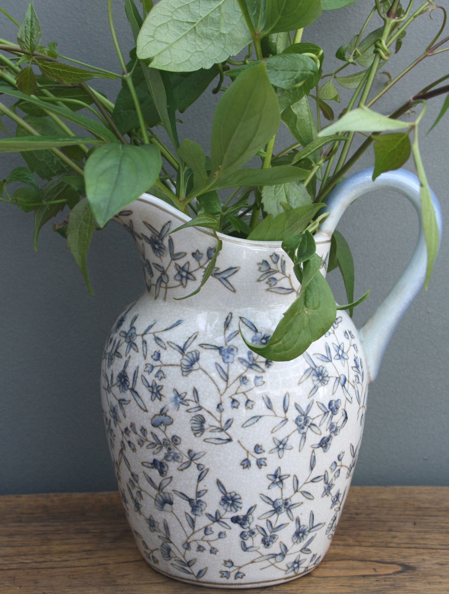 Geko Products blue and white decorative jug with floral pattern filled with green leafy plants on wooden surface