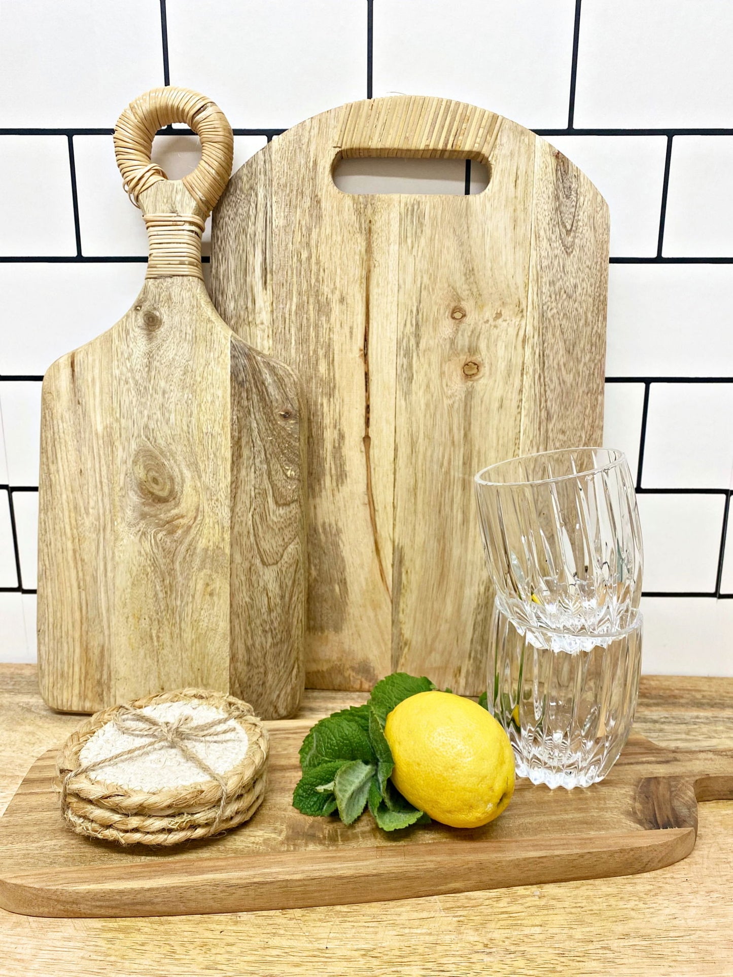 Stack of braided jute coasters next to wood cutting boards lemon mint and clear drinking glasses