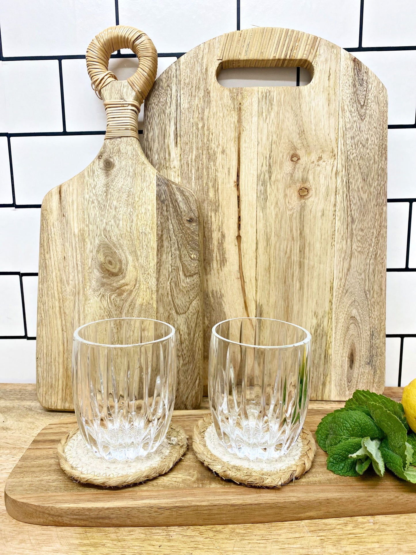 Two clear glasses on braided jute coasters with wooden cutting boards in the background