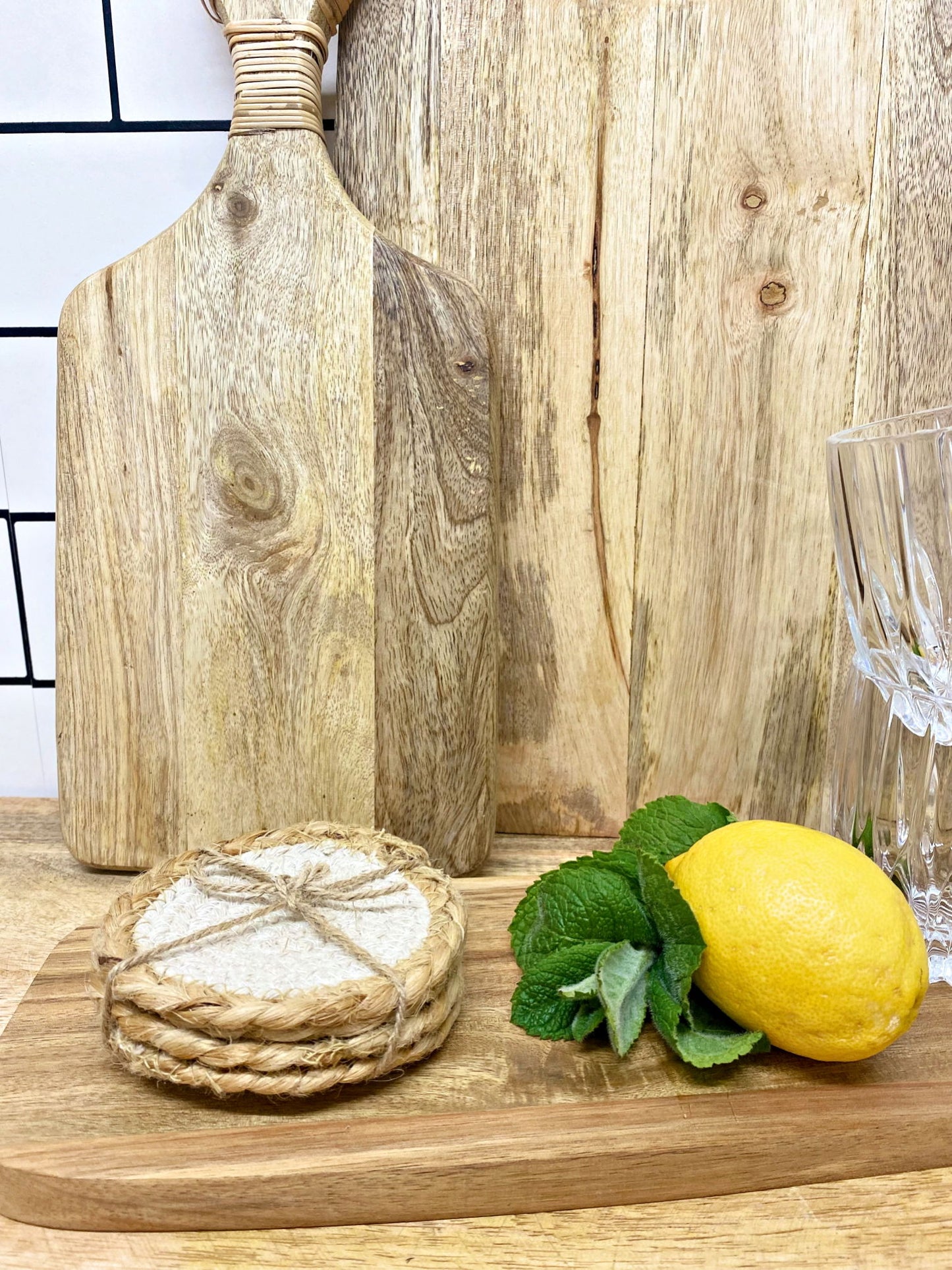 Geko Products braided jute coasters tied with twine on wooden board with lemon and mint leaves