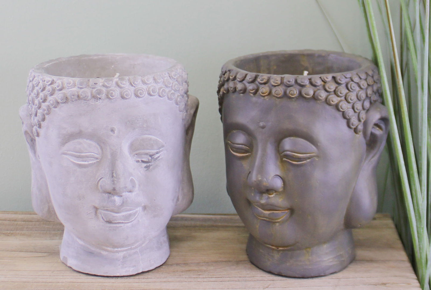 Geko Products Buddha design candles in gray and brown with detailed facial features on wooden surface