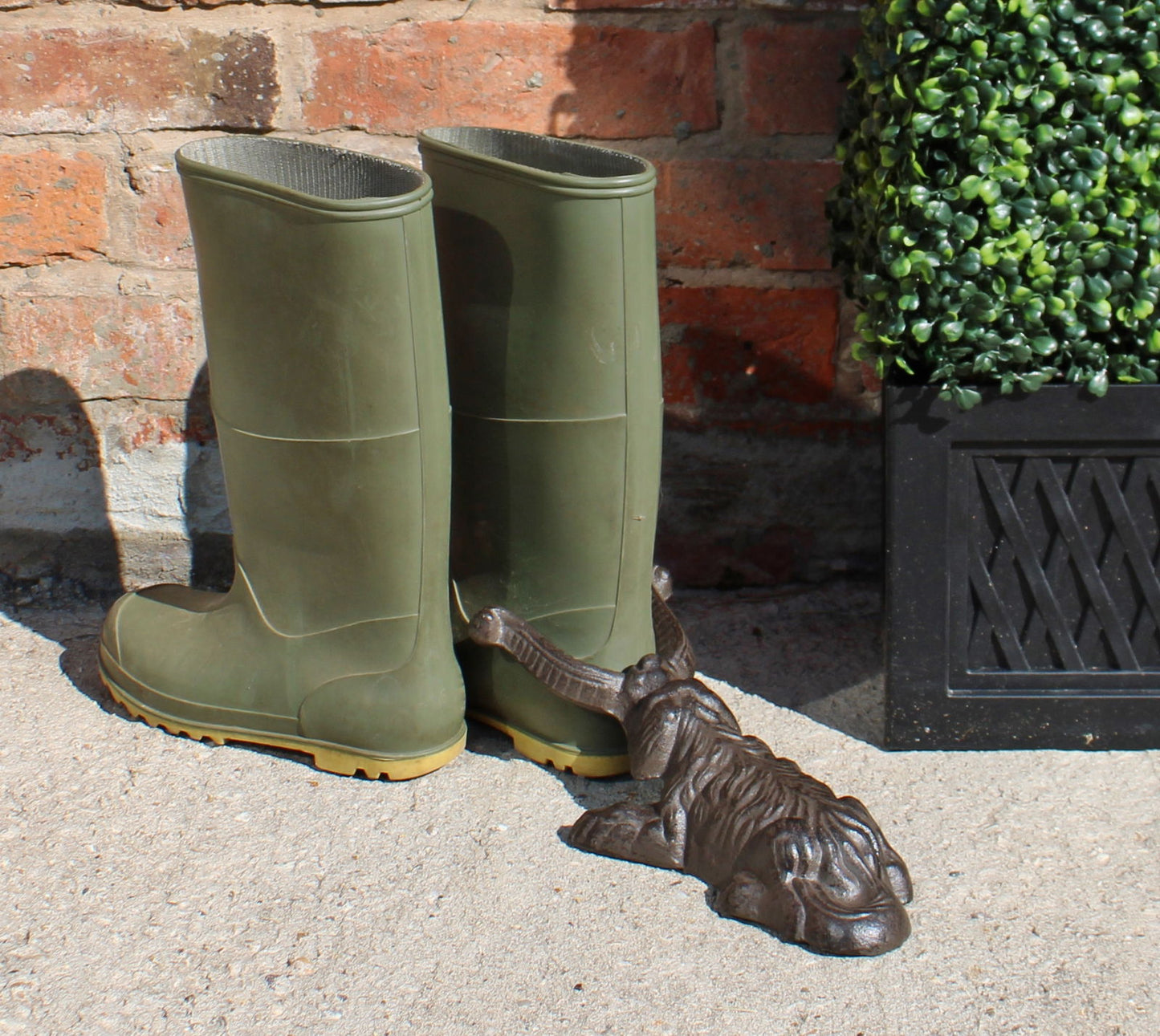 Cast iron boot jack dog design beside green rubber boots on outdoor concrete surface