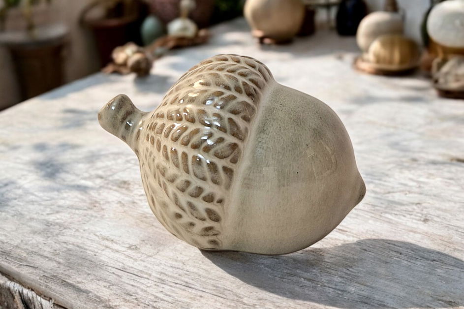 Geko Products ceramic acorn ornament with detailed textured cap on rustic wooden surface