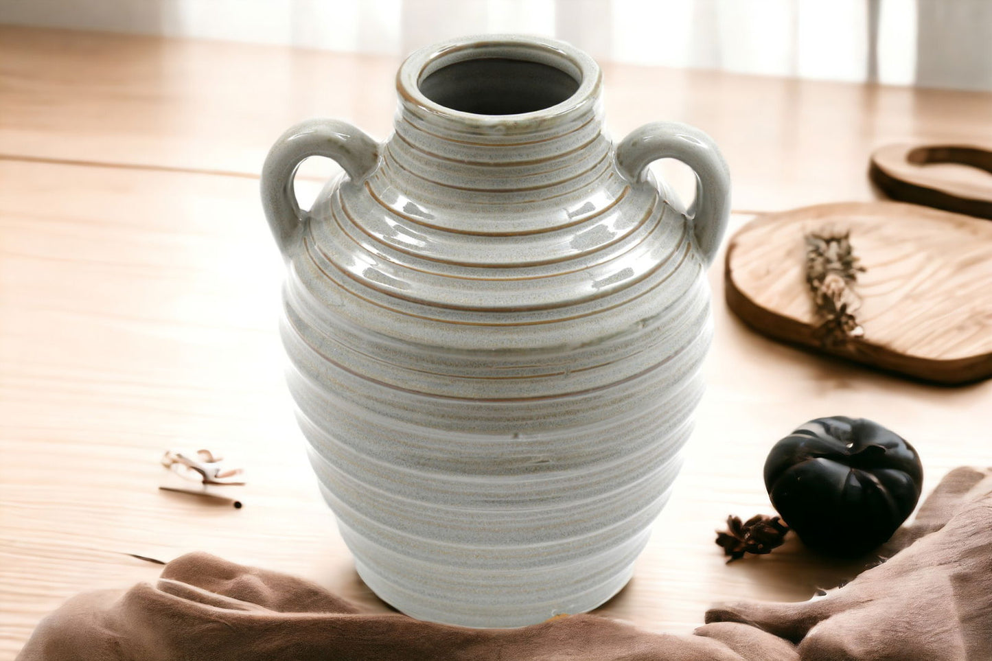 Ceramic grey ribbed vase with two handles displayed on wooden table with decorative items