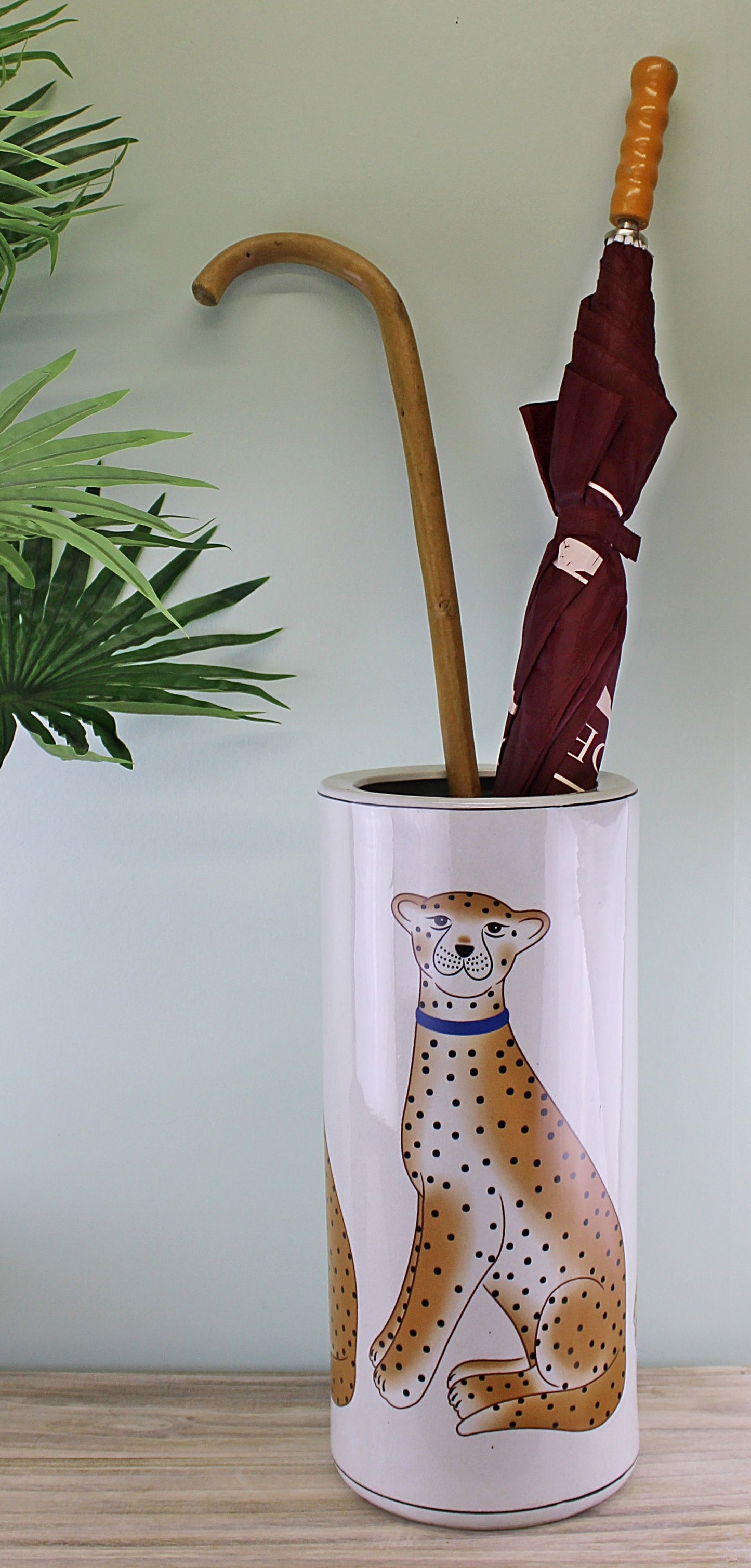 Ceramic leopard decor umbrella stand with leopard illustration holding a wooden cane and maroon umbrella