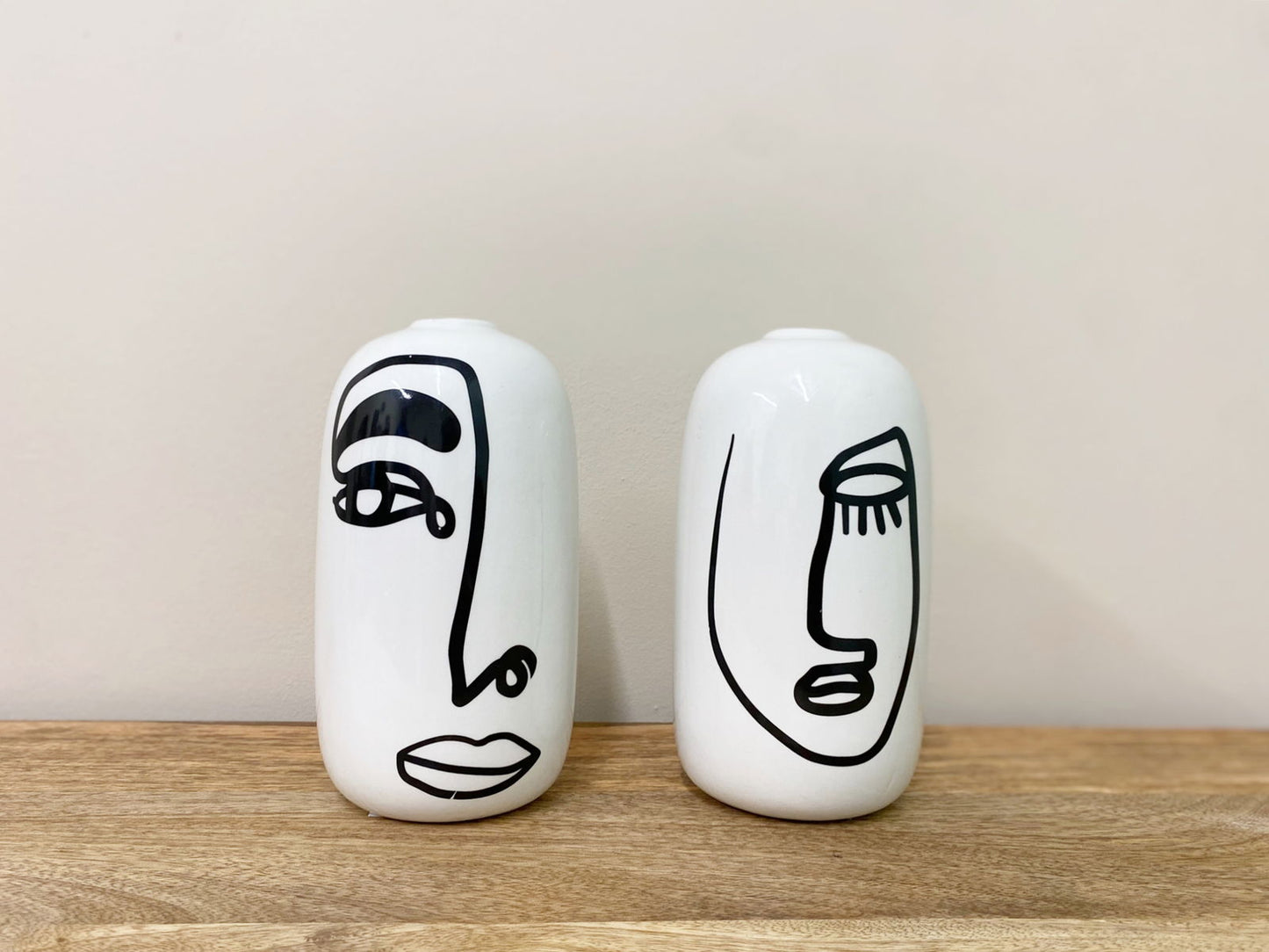 Set of two white ceramic vases with face design in black line art on wooden surface