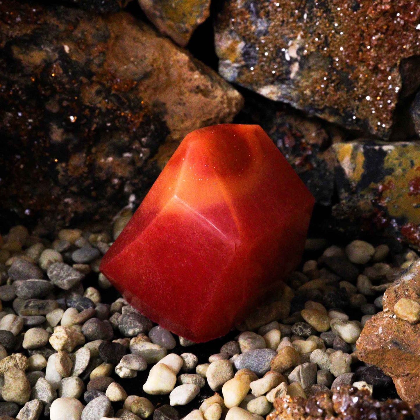 Crystal Fire Gemstone Soap in a unique red shape, displayed on pebbles against a rocky background