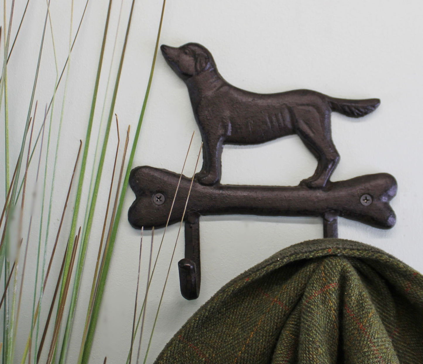Dog design metal coat hooks in dark brown holding a green coat on a white wall near decorative grass