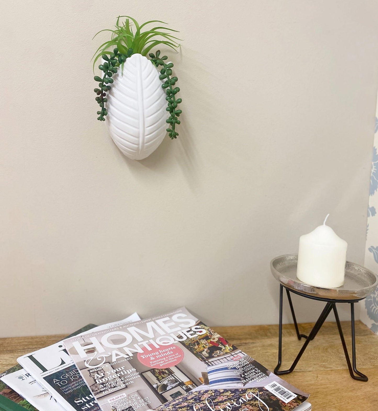 White wall vase with realistic faux succulents wall decor hanging above wooden table with magazines and candle
