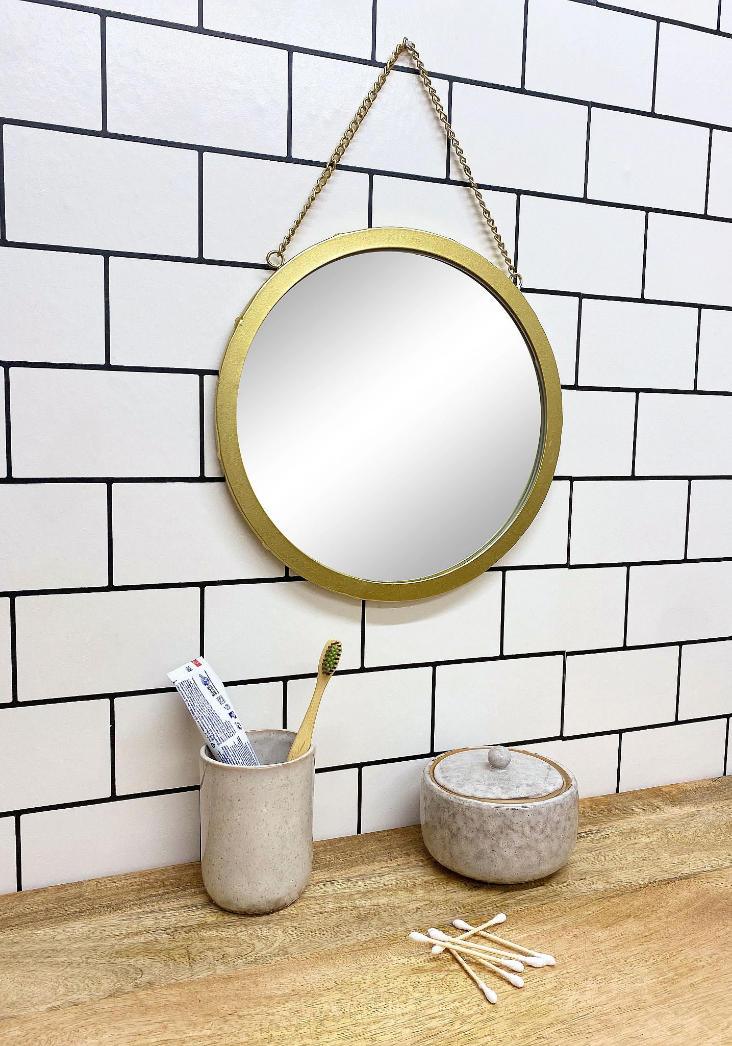 Taupe ceramic pot with lid on wooden countertop next to matching toothbrush holder in modern bathroom