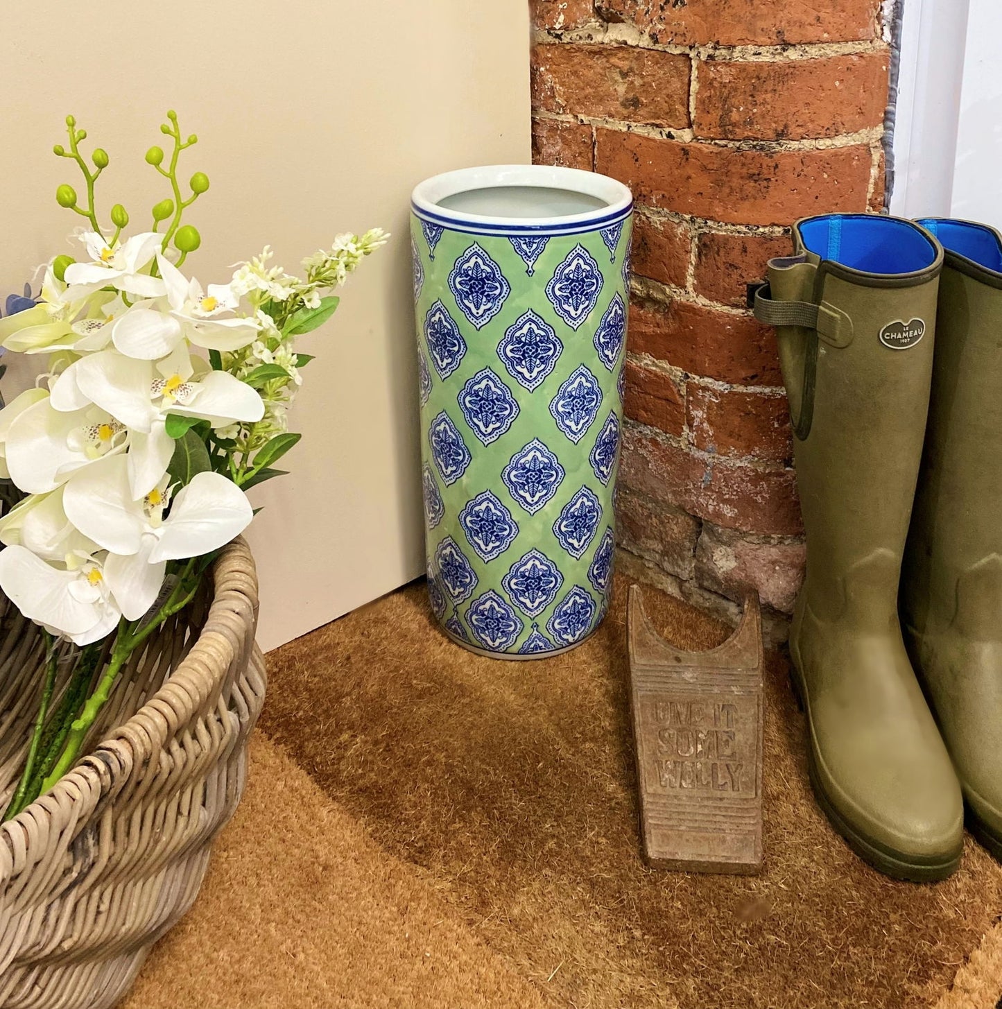 Geko Products green diamond umbrella stand with blue and white diamond pattern placed on floor near boots and floral basket