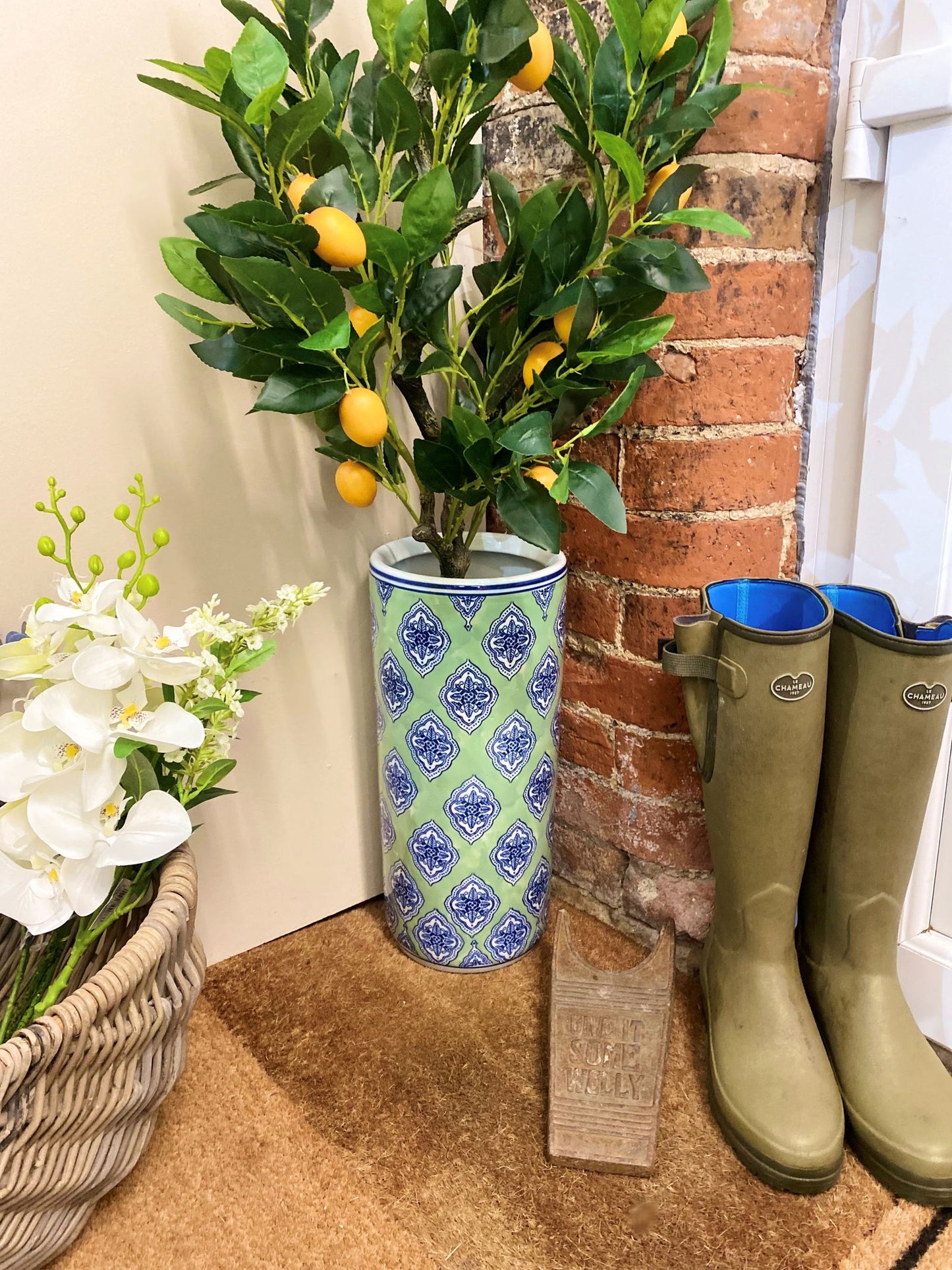 Tall green diamond umbrella stand with blue diamond pattern placed near rain boots and plants indoors
