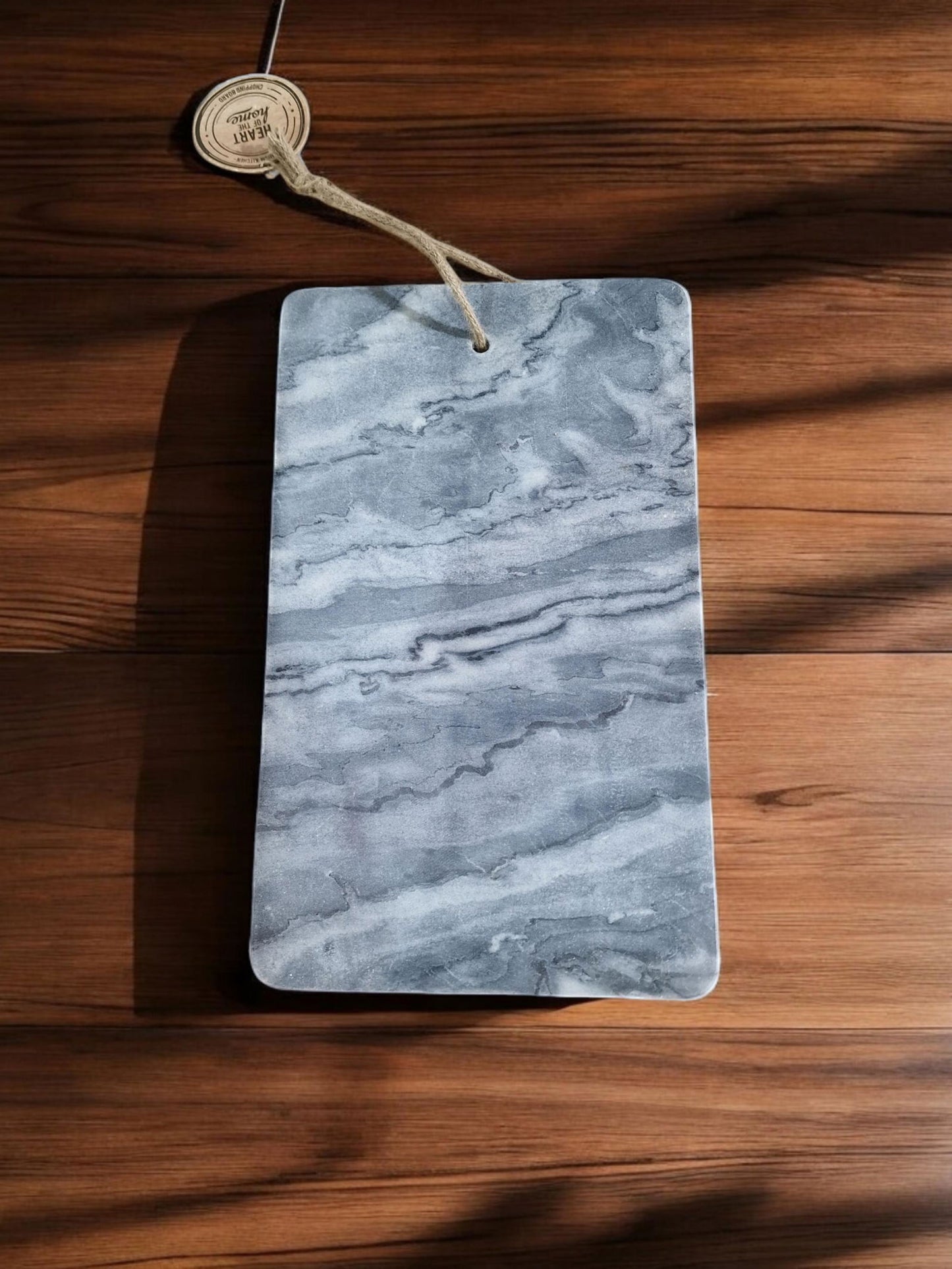 Grey marble chopping board with natural stone texture and hanging rope on wooden surface