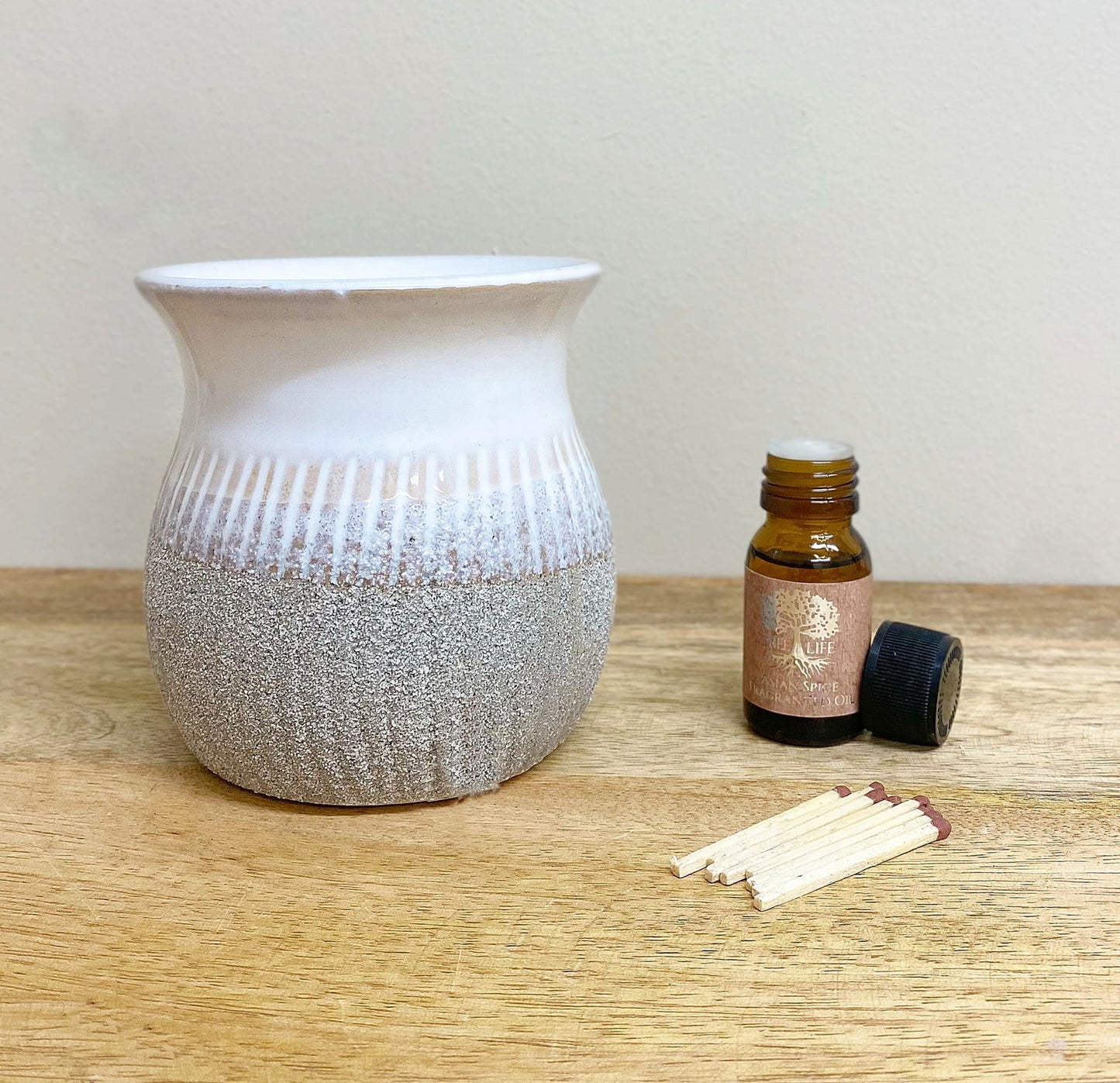 Geko Products grey sandstone oil burner with ribbed texture and essential oil bottle on wooden surface