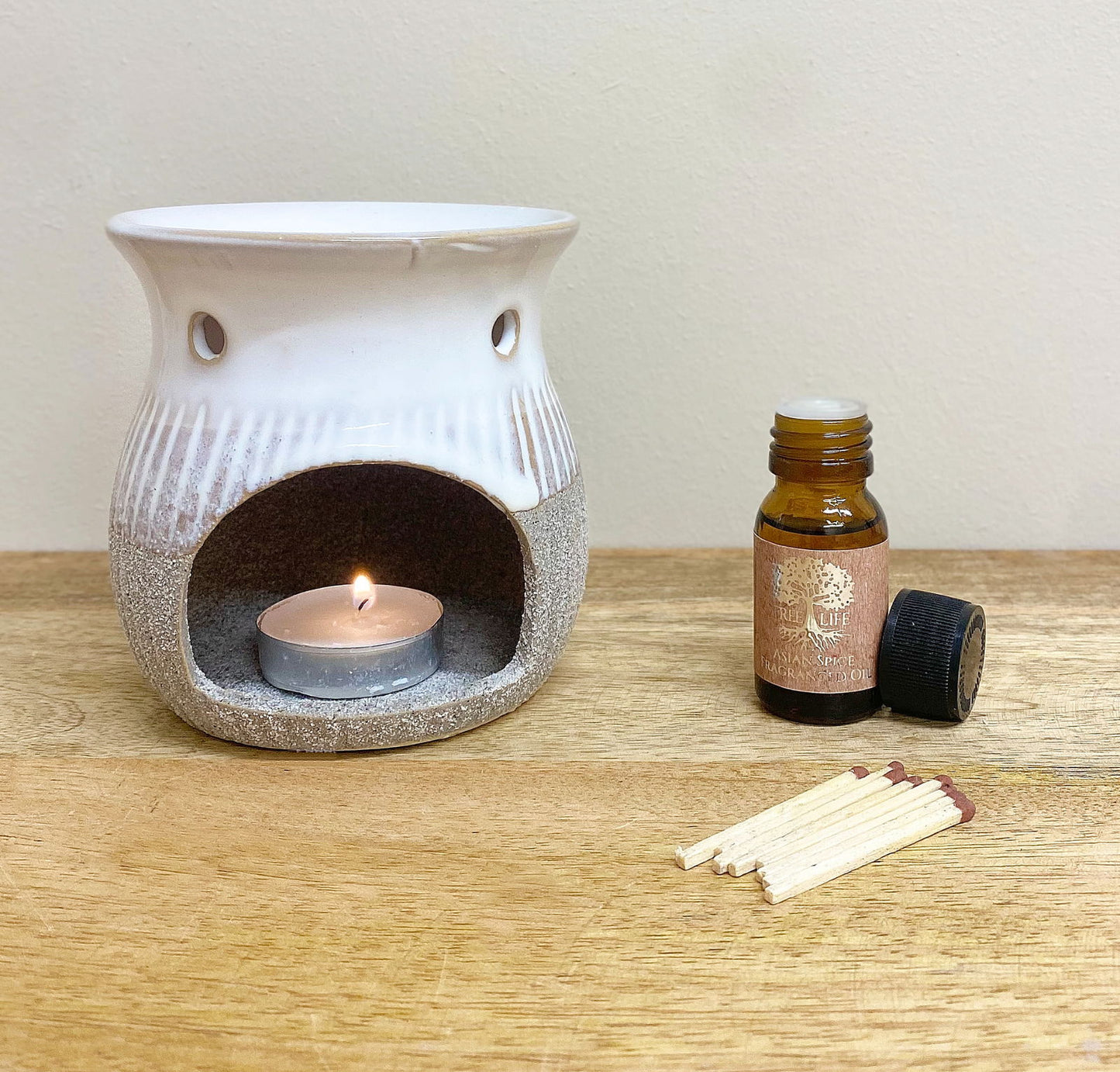 Geko Products grey sandstone oil burner with lit candle, amber essential oil bottle, and matches on wooden surface