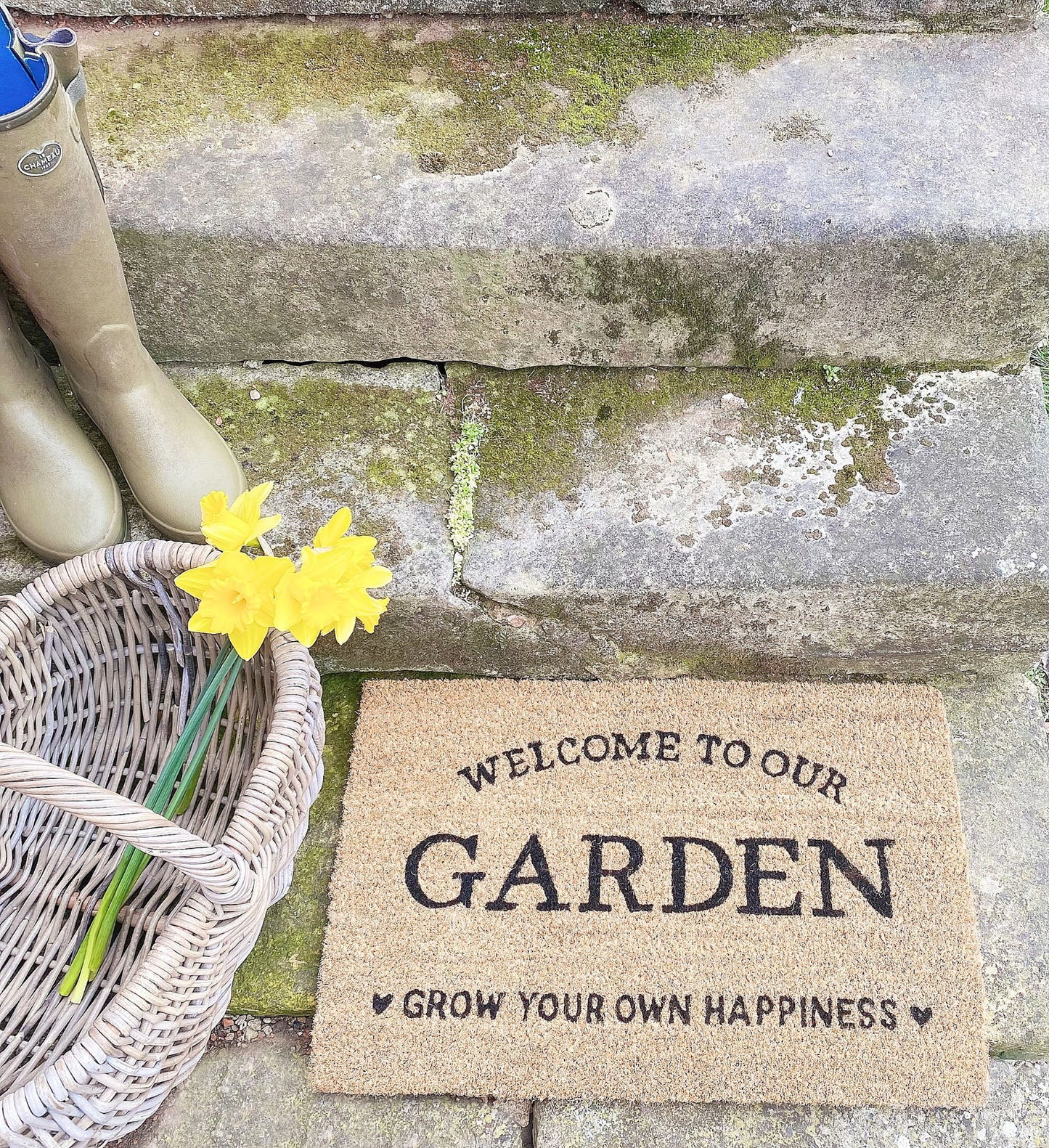 Grow your own happiness doormat with welcome to our garden text placed on stone steps with basket and yellow flowers