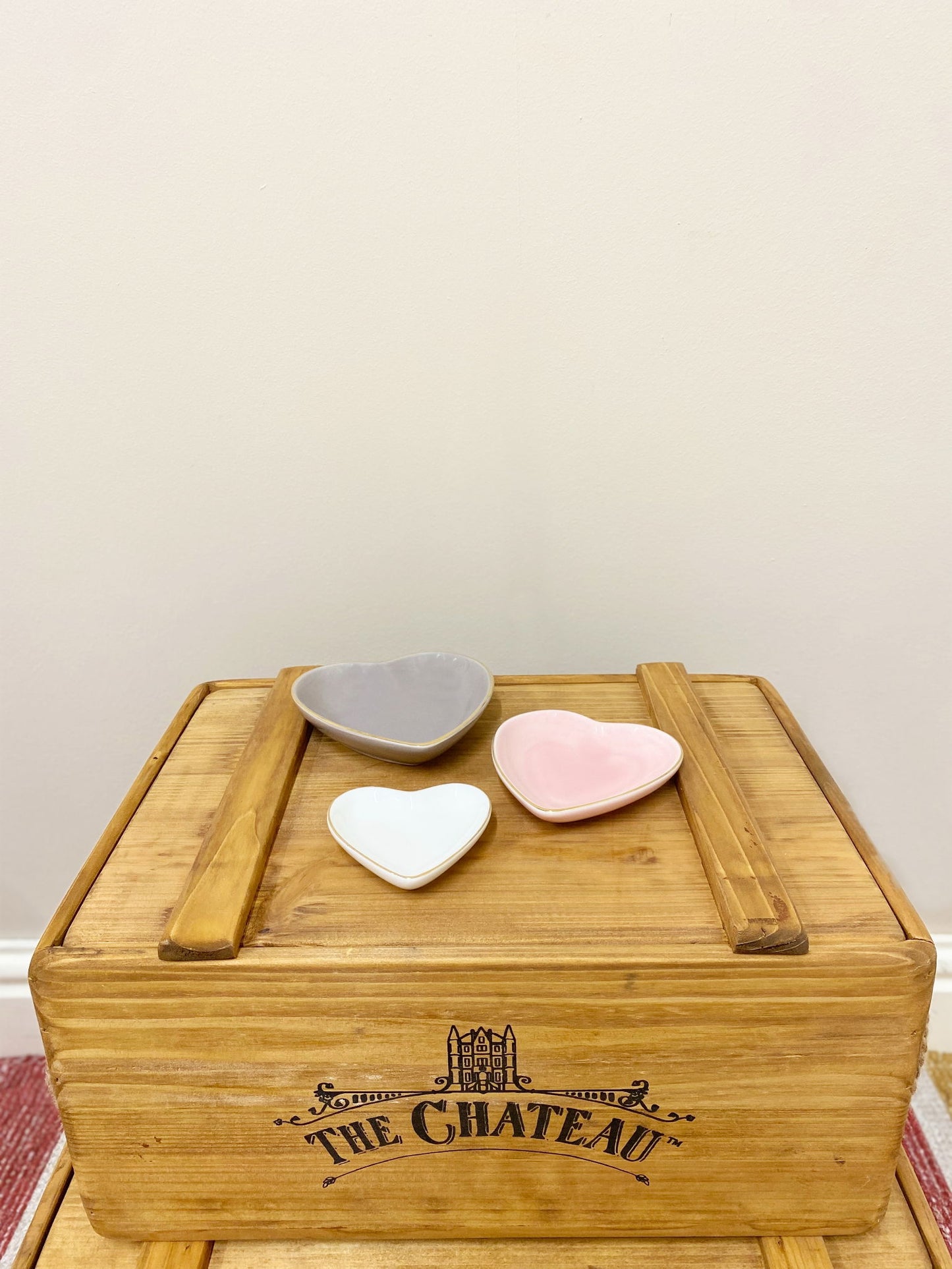 Set of three heart shaped trinket dishes in gray, pink, and white on wooden crate labeled The Chateau