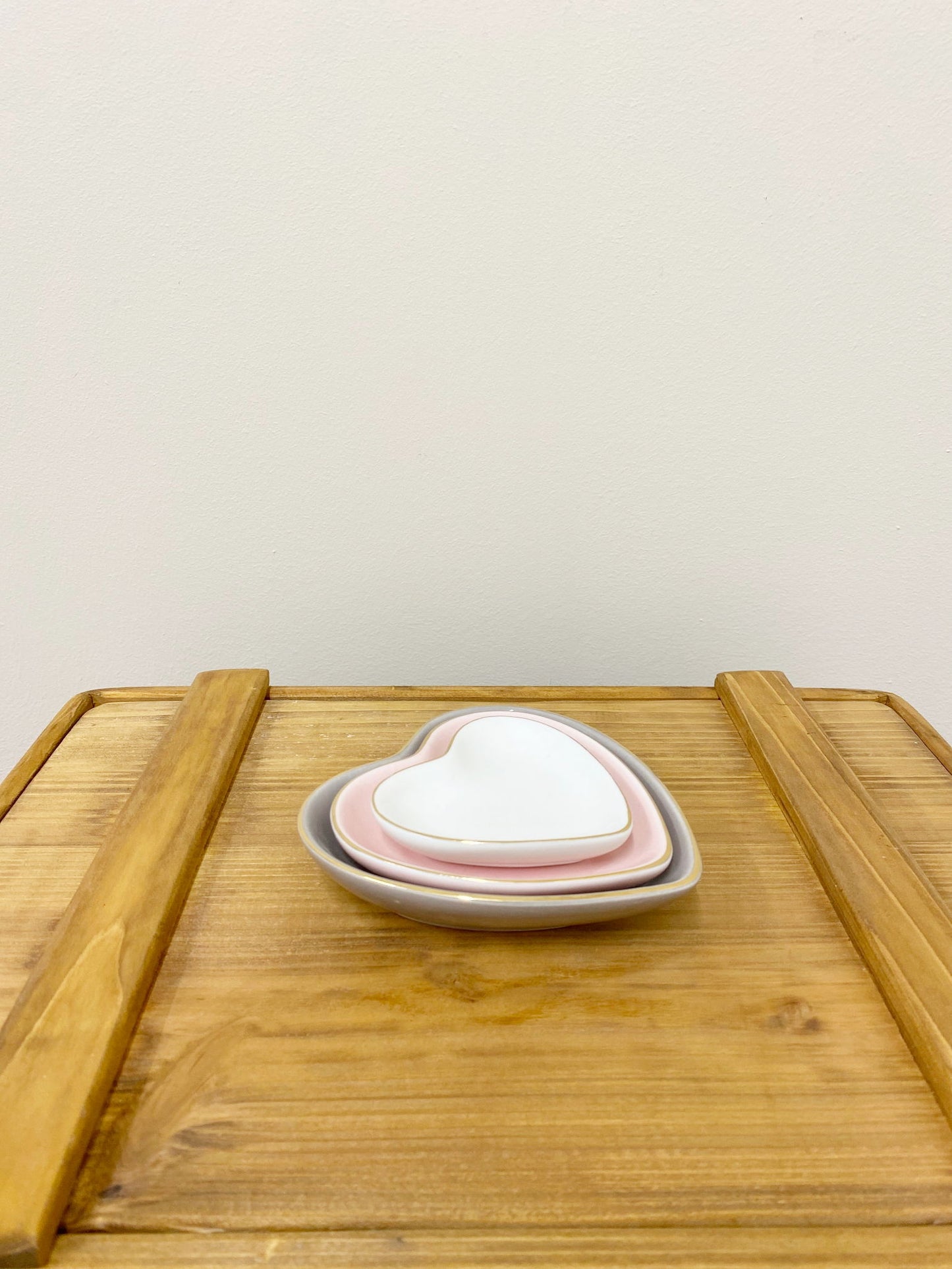 Stack of white, pink, and gray heart shaped trinket dishes on a wooden surface by Geko Products