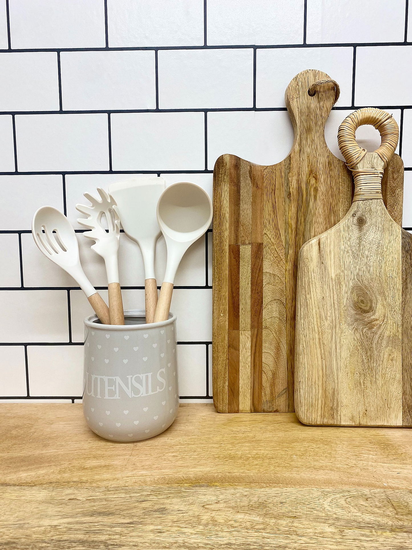 Hearts design utensil holder in gray with white utensils on wooden countertop by wooden cutting boards