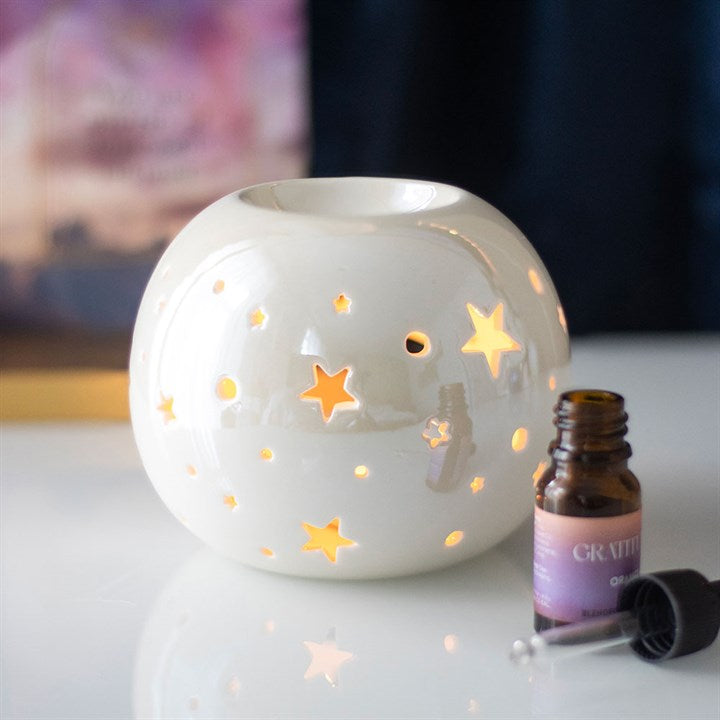 White iridescent ceramic oil burner with stars and essential oil bottle for a cozy ambiance