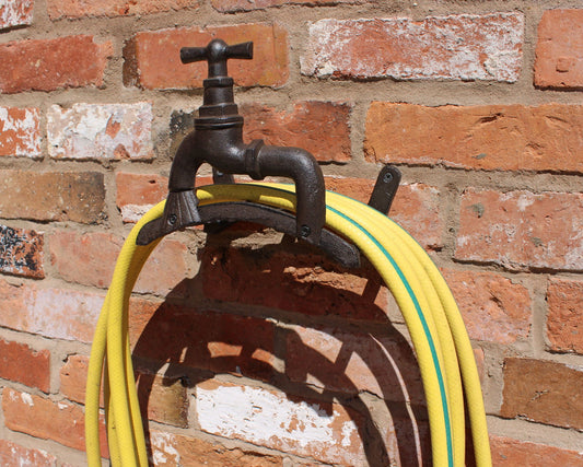 Rustic cast iron hose holder mounted on brick wall holding coiled yellow garden hose