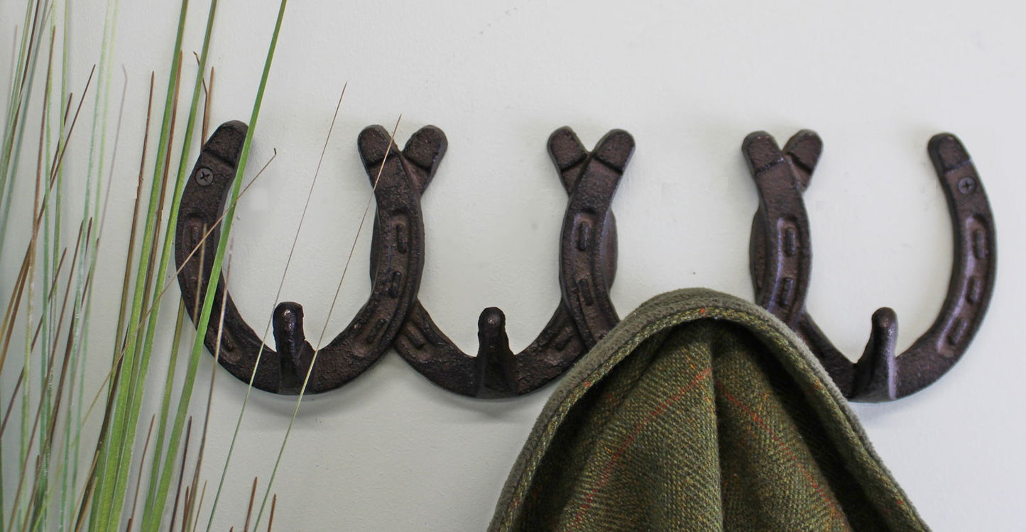 Rustic cast iron wall hooks mounted on a white wall holding a green coat with decorative grass nearby