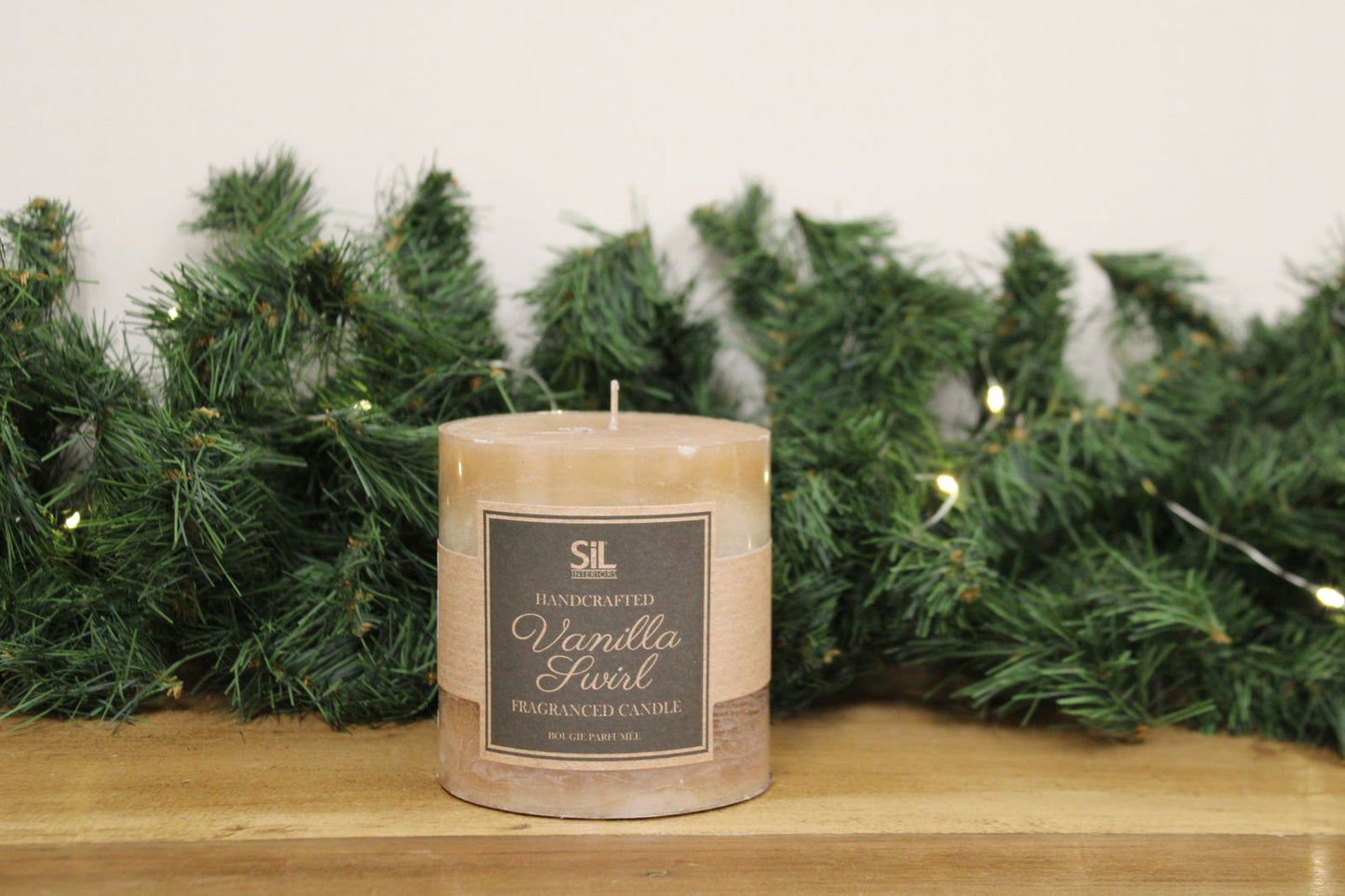 Vanilla Swirl Ombre Candle by Geko Products on wooden surface with green pine garland background