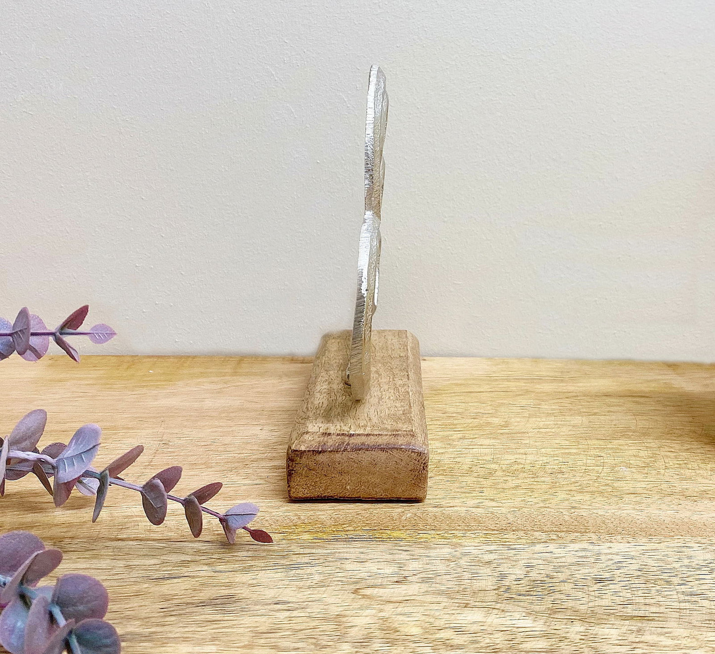 Side view of a silver heart ornament mounted on a wooden block base on a wooden surface