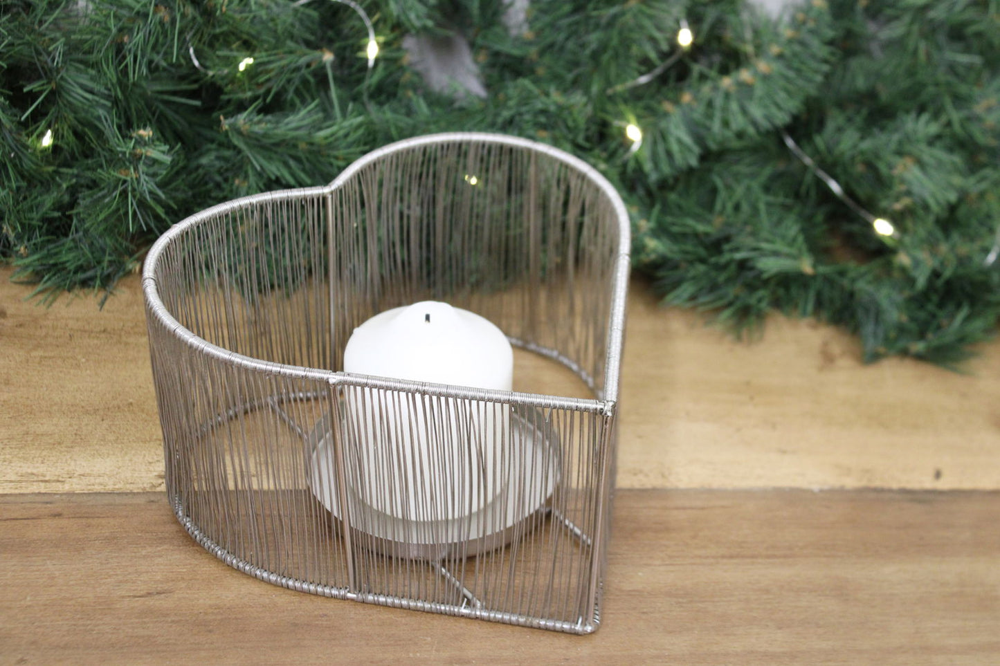 Geko Products silver heart tealight holder with white candle on wooden surface and green pine background