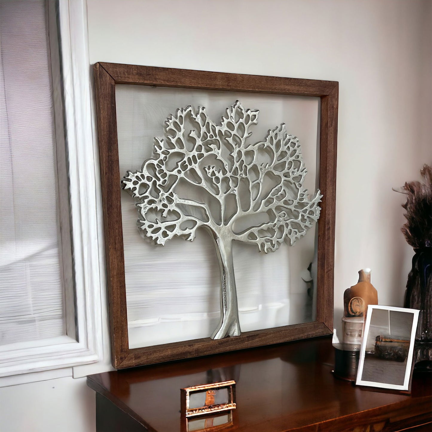 Silver Tree of Life Wall Art with wooden frame displayed on a wooden table near a window