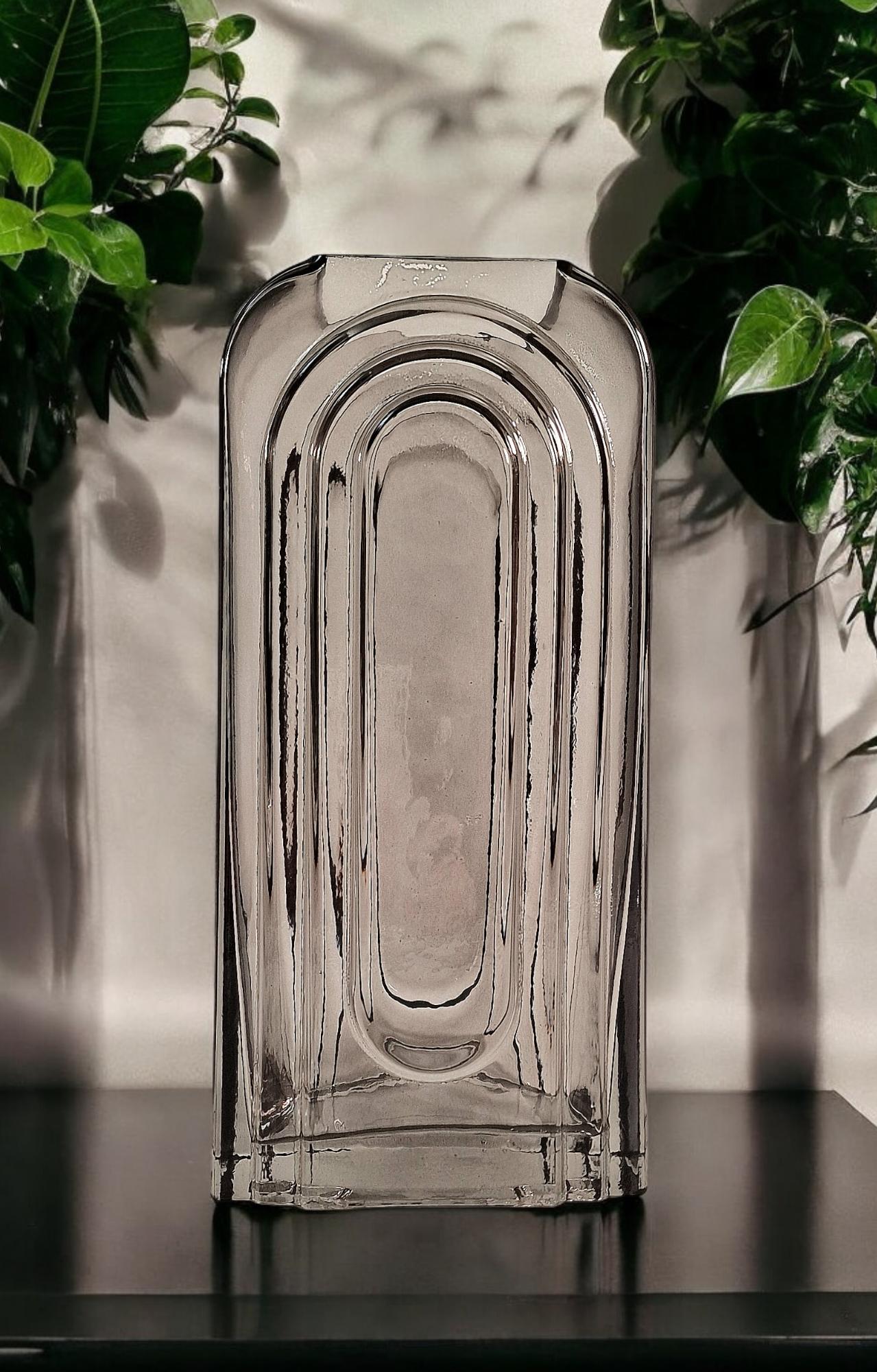Geko Products smoked glass arch vase with a modern geometric design on a black surface surrounded by green plants