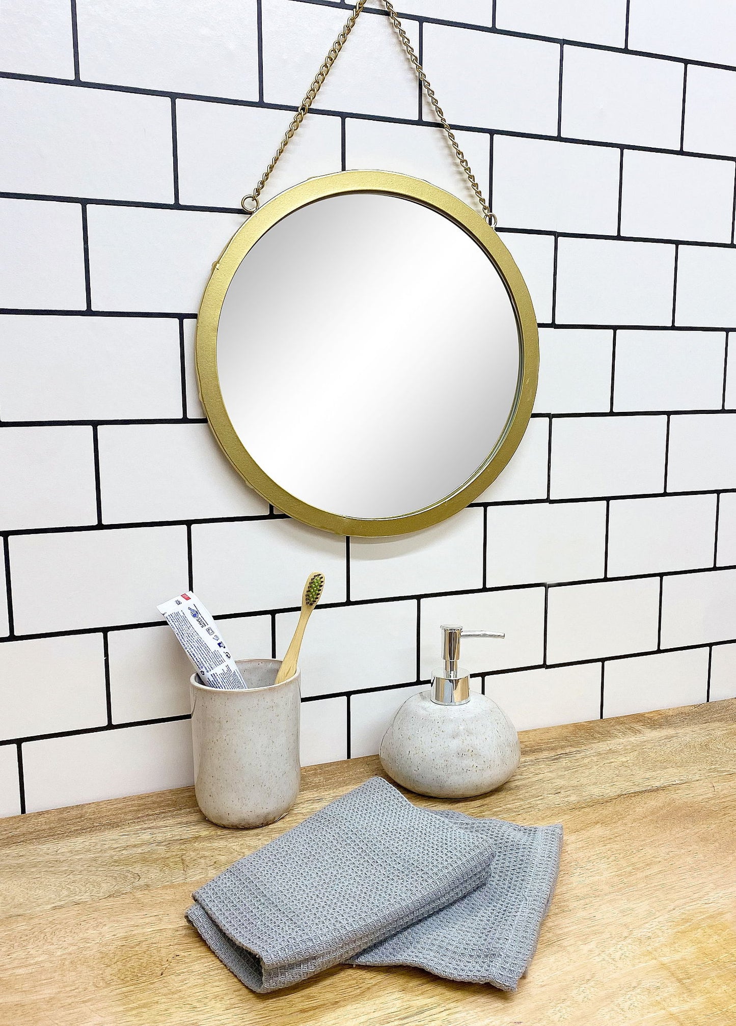 Taupe ceramic soap dispenser on wooden bathroom countertop with round mirror and towel