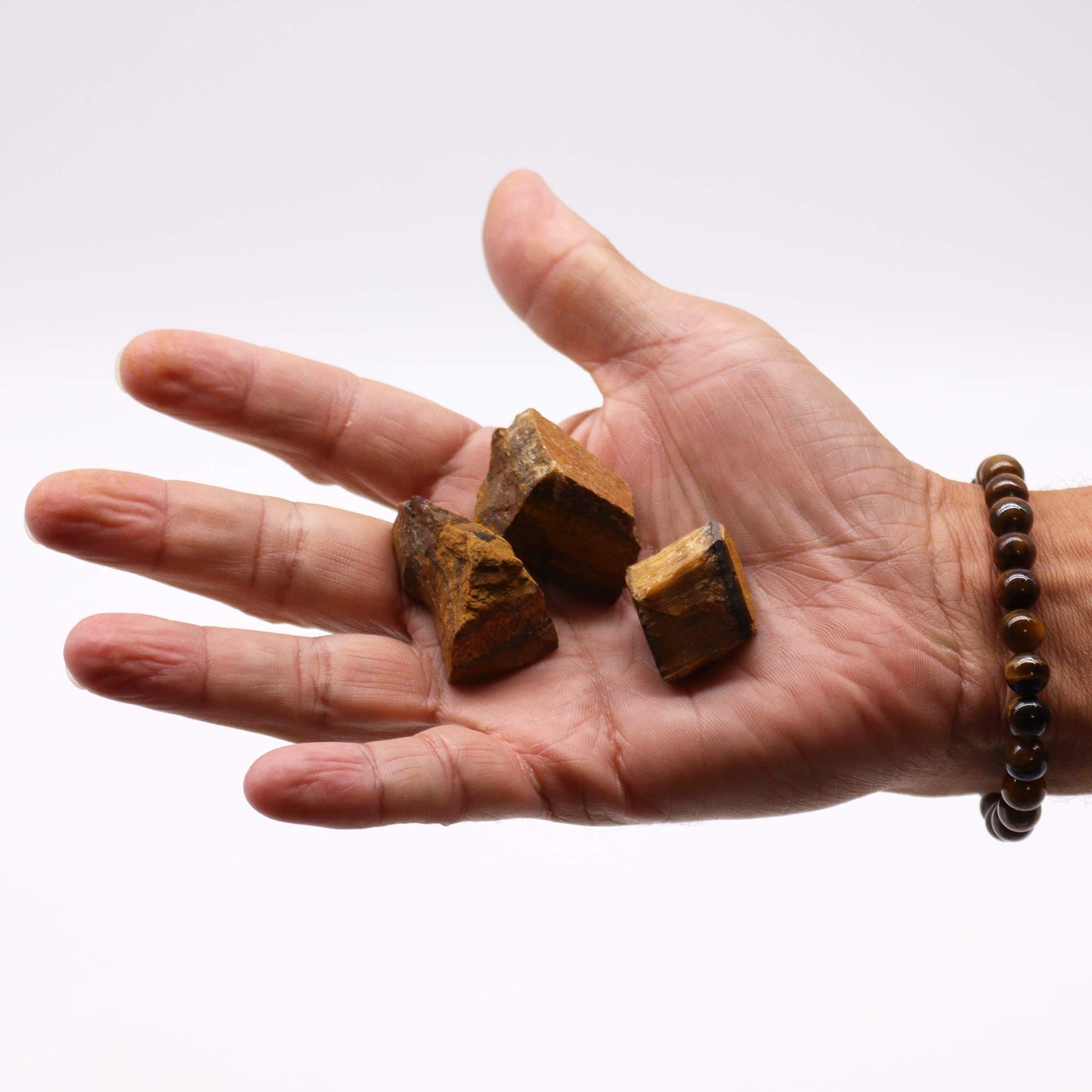 Hand holding three Tiger Eye crystals for healing showcasing their natural texture and color variations