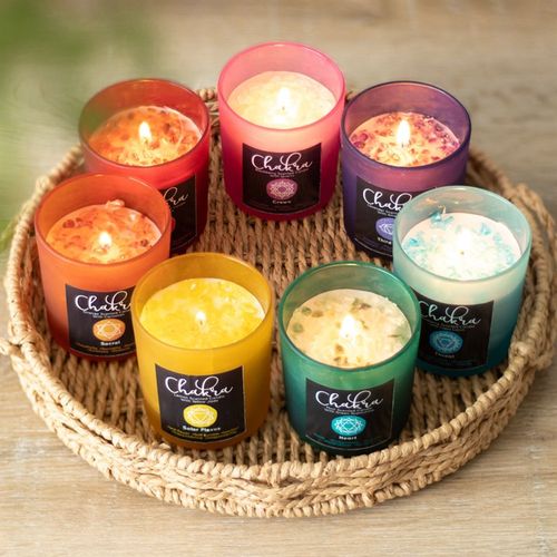 Assorted colorful candles including a root chakra strawberry crystal candle, displayed on a woven tray for spiritual wellness