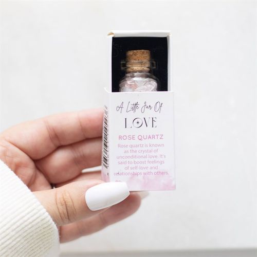 Hand holding a small jar of rose quartz in matchbox with a cork lid, promoting self-love and relationships.