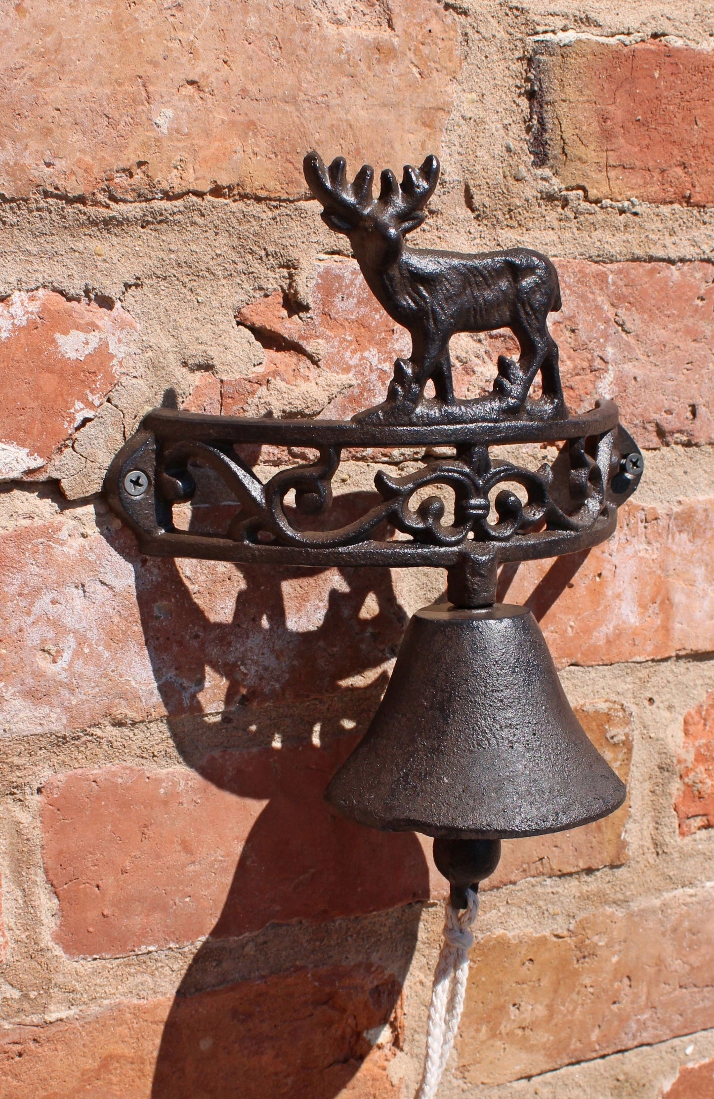 Rustic cast iron wall bell with deer design mounted on a brick wall by Geko Products