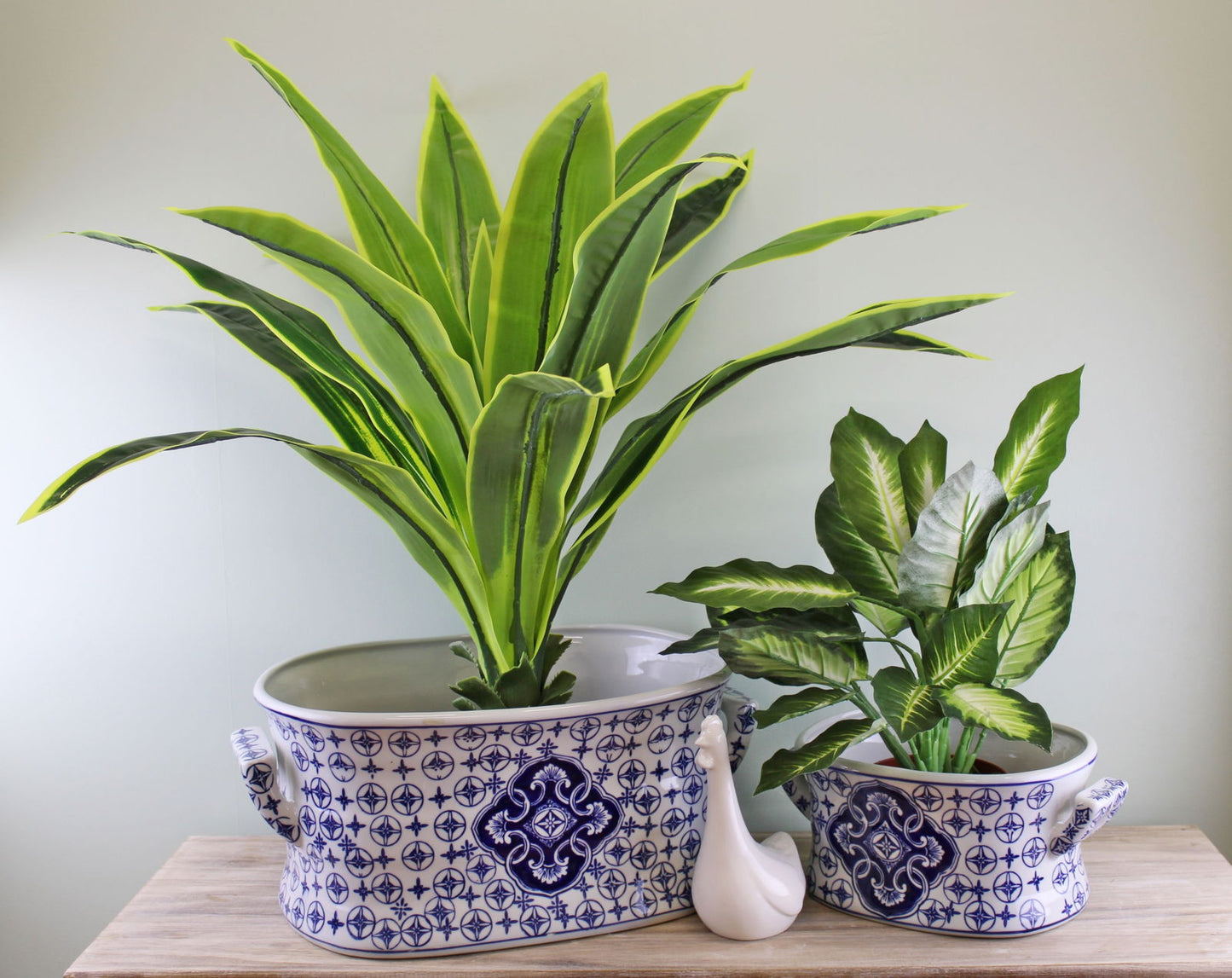 Set of vintage ceramic planters with blue patterns holding lush green plants on wooden surface