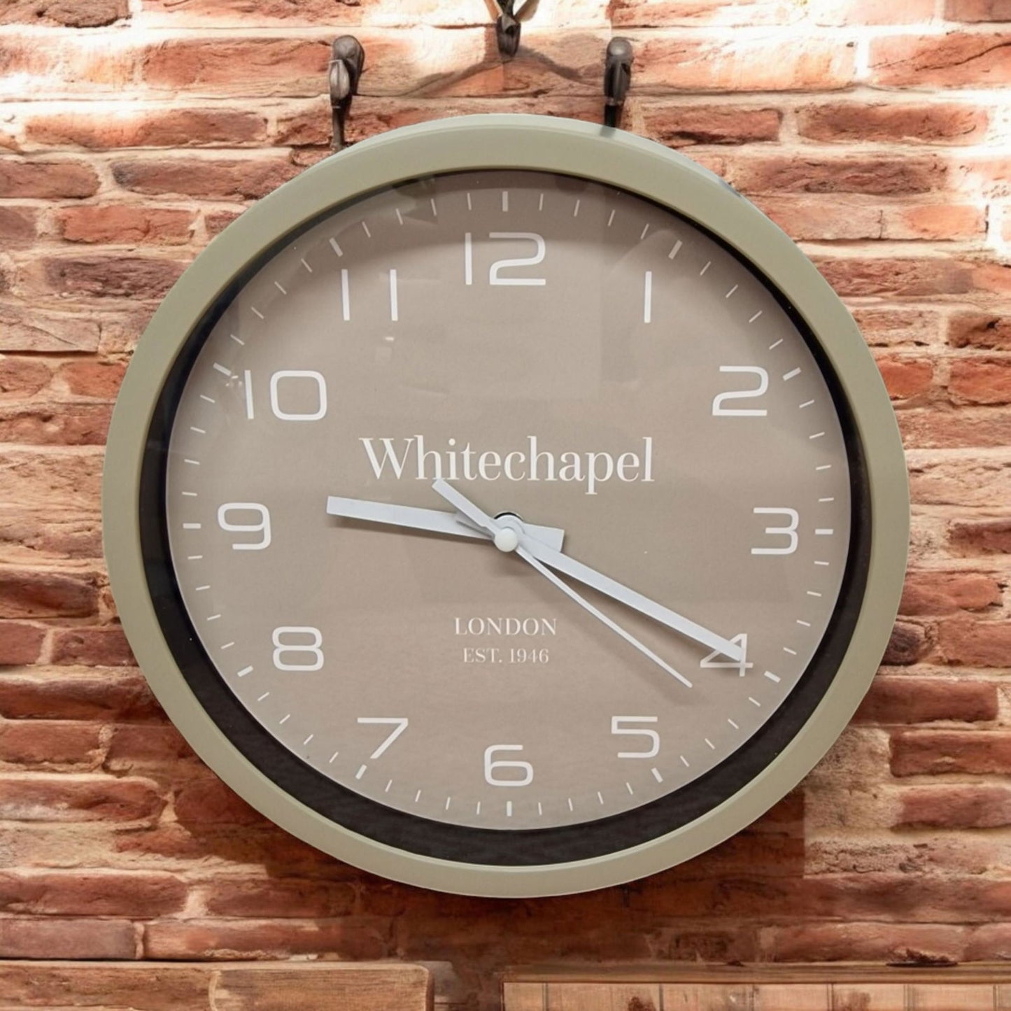 Taupe wall clock 20cm with white numbers and hands hanging on a brick wall