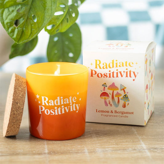 Radiate Positivity lemon candle in orange glass with cork lid, featuring colorful mushroom packaging, perfect for brightening any space.