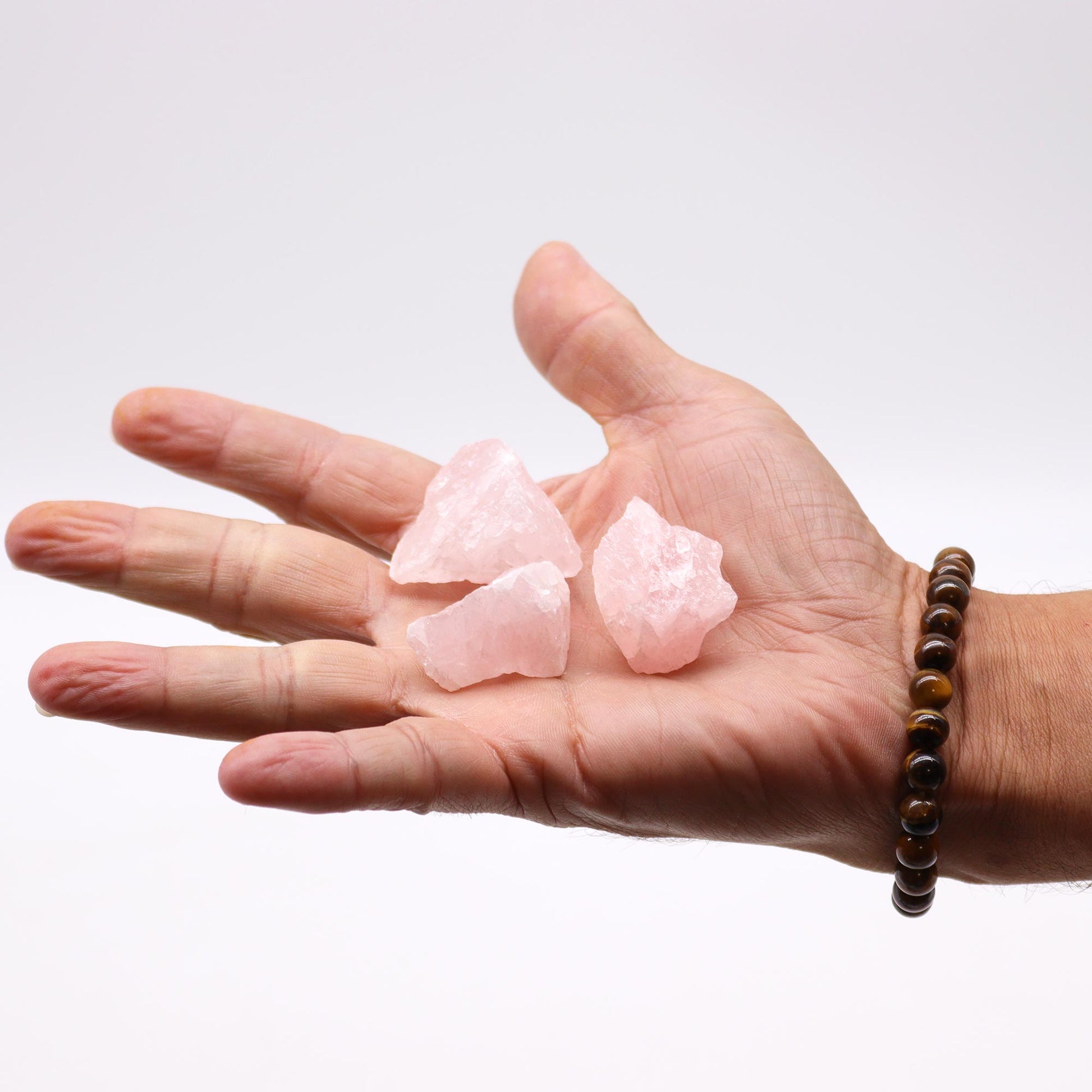 Three raw rose quartz crystals for healing displayed in a hand with a beaded bracelet