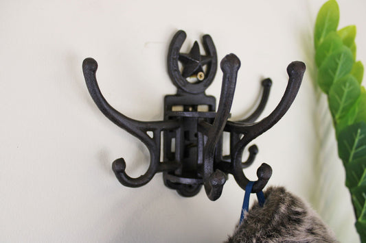 Black cast iron rotating coat hooks mounted on wall holding a fur-lined hat next to green leaves